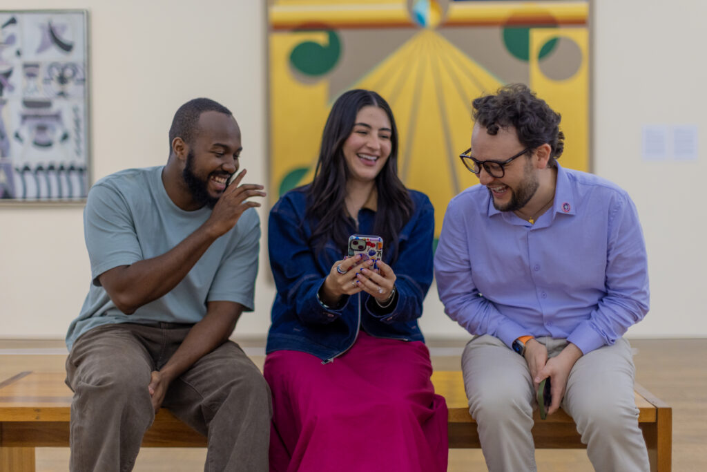 Three friends laughing in galleries looking at a phone