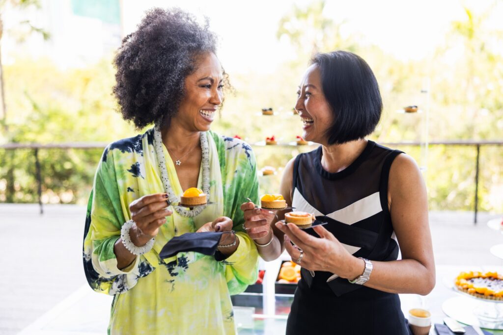 Two women holding desserts while laughing together.